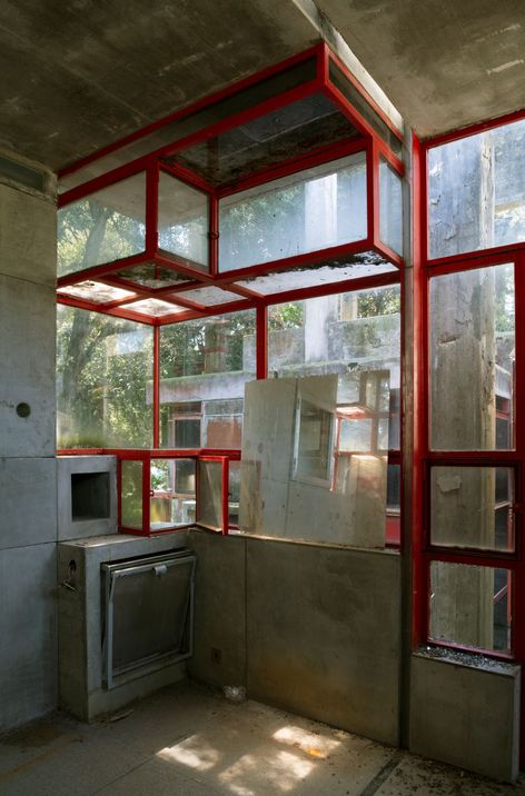 Interior with red steel frame and large windows, concrete walls and ceiling, mirror, and built-in stove