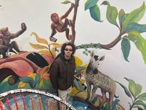 Child stands on a colorful spiral staircase in front of a wall mural depicting two monkeys, a zebra, and large leaves