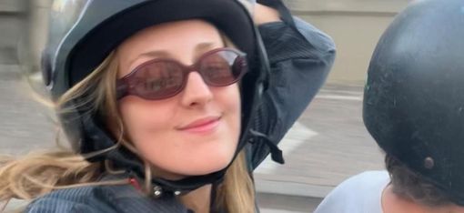 Frau mit Helm und Sonnenbrille sitzt auf einem Motorrad und lächelt in die Kamera