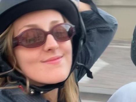 Frau mit Helm und Sonnenbrille sitzt auf einem Motorrad und lächelt in die Kamera