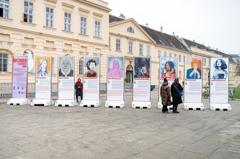 nine large information pillars with portrait photos and texts about women as part of  the exhibition  „women against war“; three women are looking at the pillars in front of the MQ.