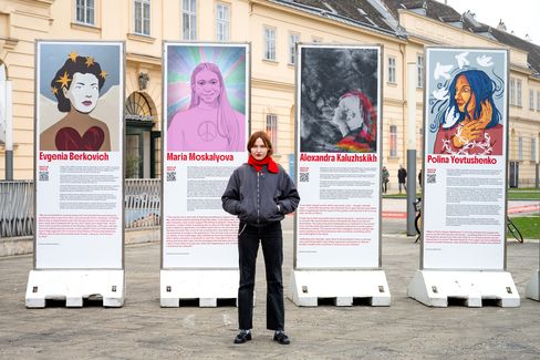 Fünf große Informationssäulen mit Porträtfotos und Texten über Frauen; eine Frau steht davor und schaut in die Kamera.