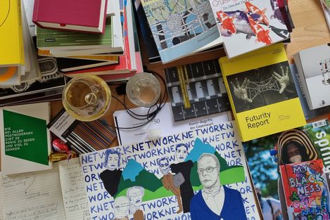 Table with several books, two glasses with drinks, and a sheet with drawings and texts including a sheet with the word "NETWORK" and several drawn people.