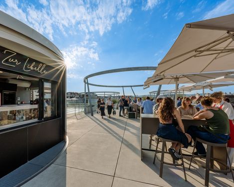 Zur Libelle bar on the roof of the Leopold Museum at MuseumsQuartier Vienna, with guests seated at tables under sun umbrellas.