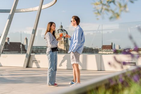 View across the lively rooftop terrace Zur Libelle at MuseumsQuartier Vienna with guests, seating areas and panoramic city views.