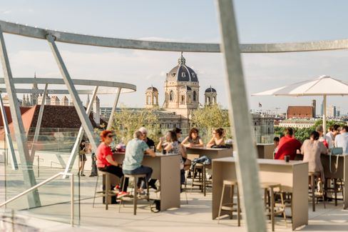 Menschen sitzen an Tischen auf der MQ Libelle. Im Hintergrund die Dächer Wiens.