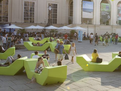 Menschen sitzen und entspannen auf grünen Enzi-Sitzmöbeln im Innenhof des MuseumsQuartier Wien, im Hintergrund die Kunsthalle Wien, Caféterrassen und sommerliches Treiben unter Bäumen.