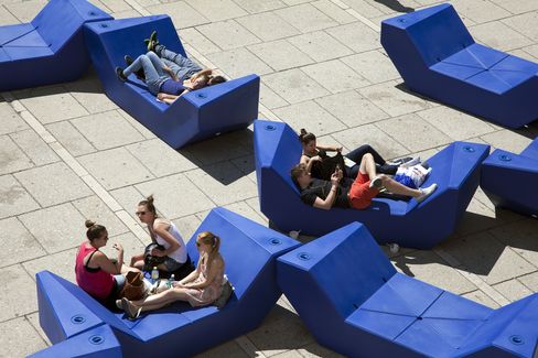 People relaxing on blue Enzi seating at MuseumsQuartier Vienna, sitting or lying in small groups on the paved courtyard.
