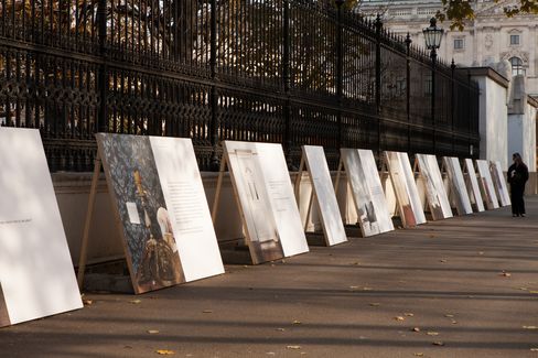 Several large panels with images and text leaning against an iron fence along a sidewalk with a person standing at the right edge.
