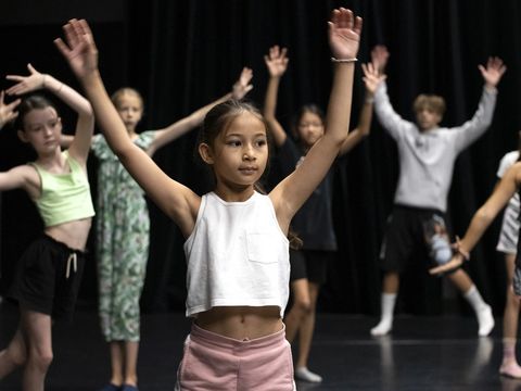 Kinder stehen mit einem zum V erhobenen Armen auf einem Tanzboden.