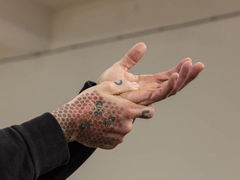 Two tattooed hands, one hand holding the other from below.