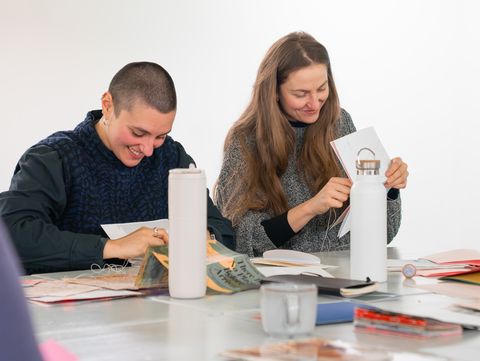 Zwei Personen nehmen an einem Künstler*innenworkshop im Kunsthalle Wien Atelier teil und binden Bücher.