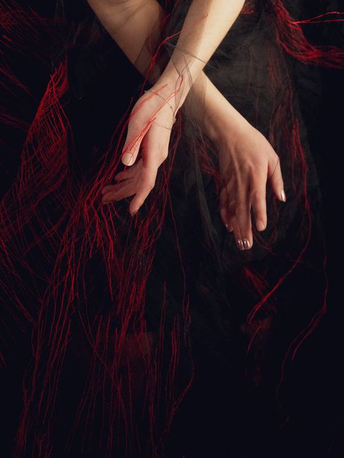 Two crossed hands against a dark background with red threads winding around the arms