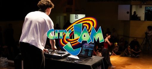 A person can be seen standing at a mixing desk from behind. Children are sitting at the edge of the dance floor, watching a person step onto the floor. The words "City Jam" are positioned in the centre of the photograph.