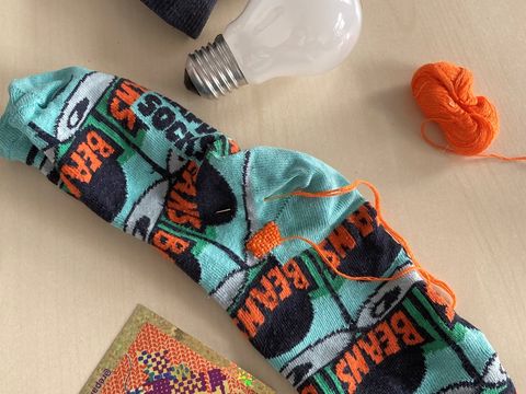 Two colorful socks with the word "BEAMS" lie on a light surface next to a light bulb and a small ball of orange yarn.