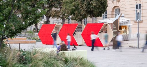 Three large red arrows on a plaza with people and trees in the background