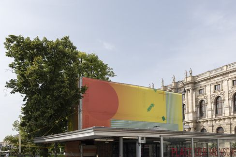 Large rectangular mural with an abstract pattern of color fields and lines on a flat roof in front of a tree and historic building.