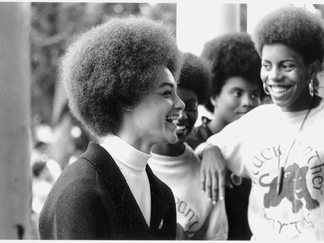 Vier Personen mit Afrofrisuren stehen nah beieinander, zwei tragen T-Shirts mit dem Schriftzug 'Black Panther Party' und einem Panther-Logo