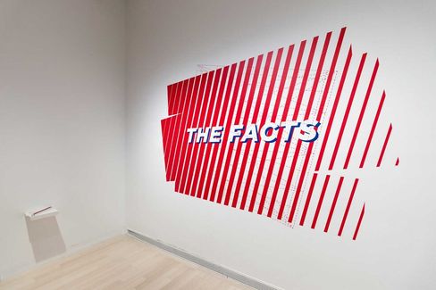 Weiße Wand mit rotem, gestreiftem Wandbild und weißem Schriftzug "THE FACTS" in einem hellen Raum mit Holzfußboden.