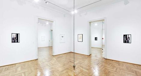 Galerieraum mit weiß gestrichenen Wänden, Parkettboden und mehreren gerahmten Bildern an den Wänden.