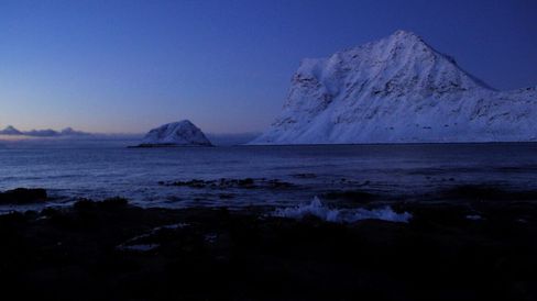 Snow-covered mountains by the sea at dusk with dark water in the foreground