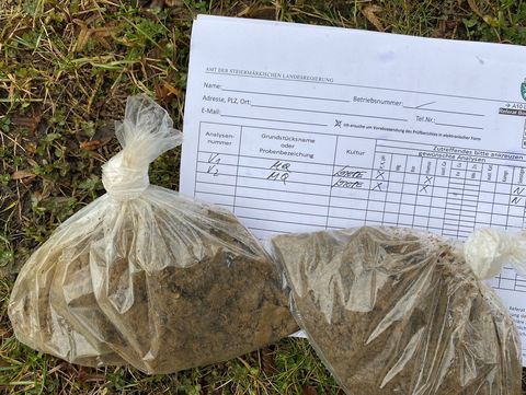 Two transparent plastic bags filled with soil lie on grass next to a filled-out soil analysis form.