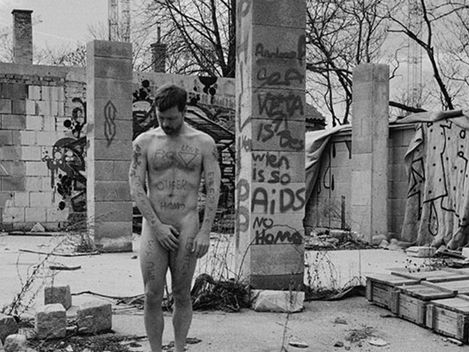 Naked man standing in an abandoned construction site covered with graffiti covering his genitals with his hands