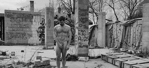 Naked man standing in an abandoned construction site covered with graffiti covering his genitals with his hands