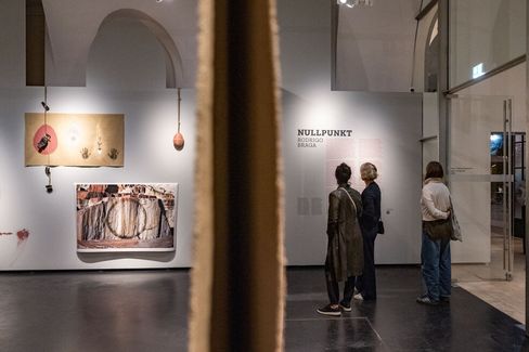 Three people looking at artworks and texts on a gallery wall with a vertical partition in the foreground