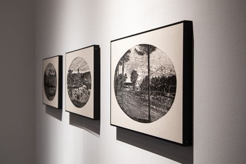 Three black-and-white line drawings with circular landscape motifs hang side by side on a white wall.