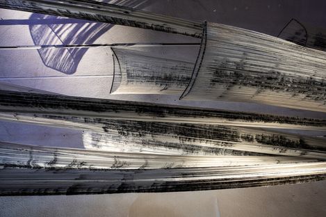 Dynamic, abstract art installation of curved, elongated metal structures with textured black and white patterns, casting shadows on a light wall.