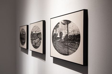 Three black-and-white line drawings with circular landscape motifs hang side by side on a white wall.
