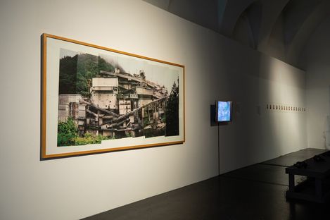 Large-format photograph of a multi-level building complex with stairways on a white wall in an exhibition