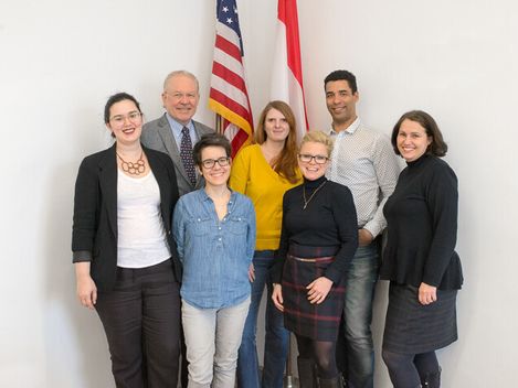 Gruppe von sieben Personen steht vor einer weißen Wand mit einer US-amerikanischen und einer kanadischen Flagge
