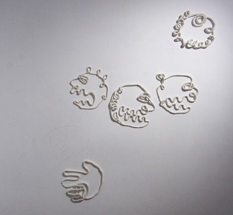 Porzellanlinien in Form von stilisierten Gesichtern und einer Hand an einer weißen Wand.