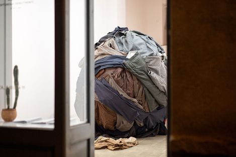 Large sphere made of compressed clothing in a room seen through an open door with a potted cactus visible on the left.