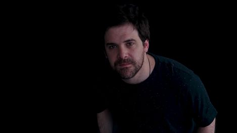 Portrait of a man with dark hair and beard against a black background.