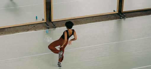 Eine Frau tanzt in einer Turnhalle vor einem Spiegel.