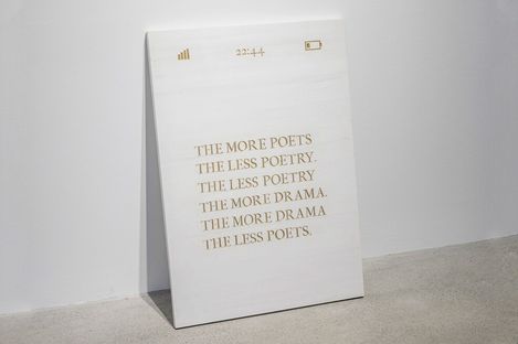 White poster with gold uppercase text reading "THE MORE POETS THE LESS POETRY THE LESS POETRY THE MORE DRAMA THE MORE DRAMA THE LESS POETS" with small icons for signal, time "22:44", and battery at the top.