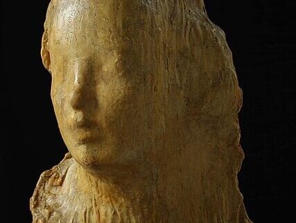 Sculpture of a female head and upper torso made of irregularly textured light brown material against a black background.