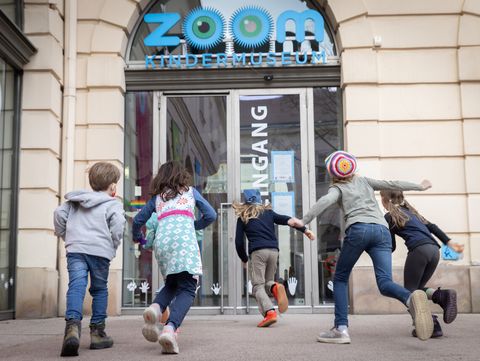 Five children running toward the entrance of the Zoom Children's Museum in a historic building.