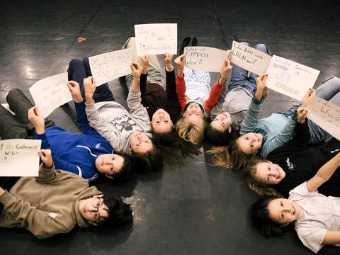 Nine children are lying on their backs in a semicircle. They are holding up questions they have written themselves.