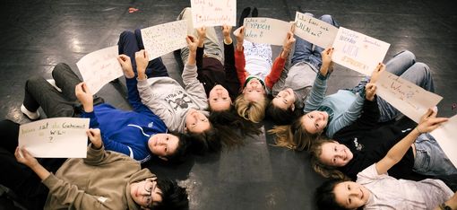 Nine children are lying on their backs in a semicircle. They are holding up questions they have written themselves.