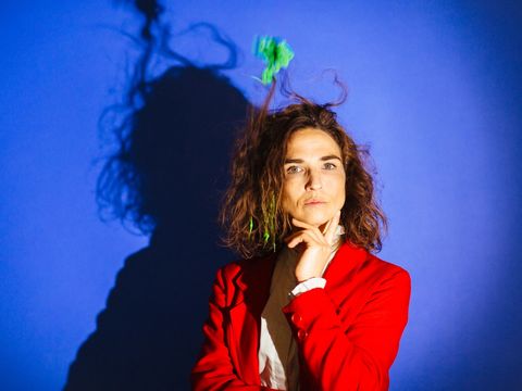 A woman in a red jacket is looking at the camera. Her hair is standing on end because a green thing is whirling it about.