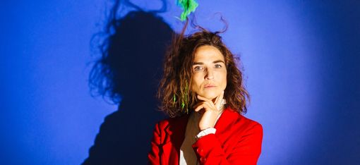 A woman in a red jacket is looking at the camera. Her hair is standing on end because a green thing is whirling it about.