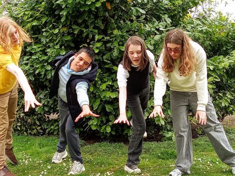 Four young people are standing in a meadow. Their gestures can be interpreted as reaching out for something invisible – a dream.