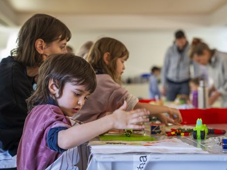 Kinder und Erwachsene sitzen an einem Tisch und gestalten Drucke.