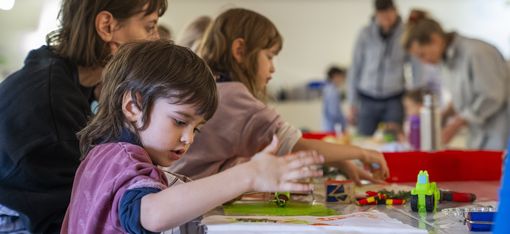 Children and adults sit around a table creating prints.