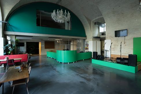 Large function room with a green reception area, a stage, microphones and a chandelier, as well as coffee tables