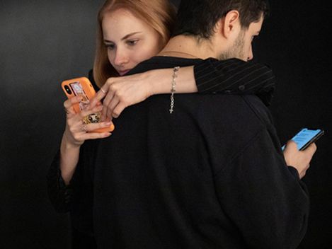 Zwei Personen stehen Rücken an Rücken, beide halten ein Smartphone in der Hand.